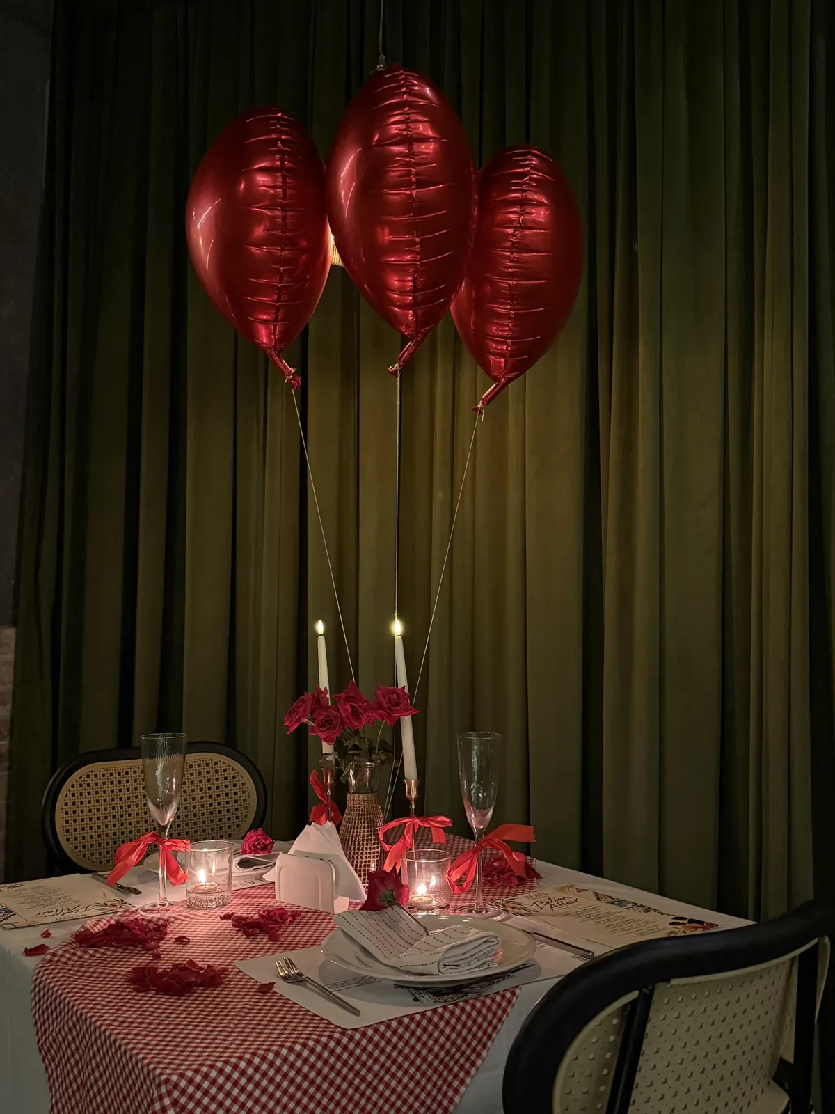 A Date Club table set with candles, roses and heart balloons against green curtains
